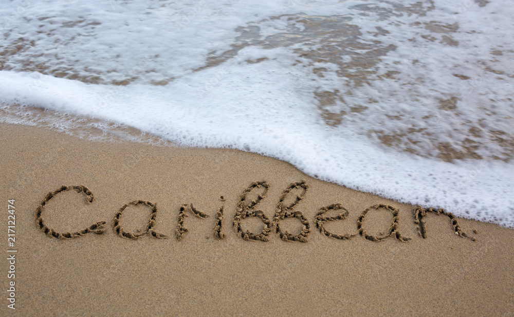 Fototapeta premium Word Caribbean written on the sand near the sea.