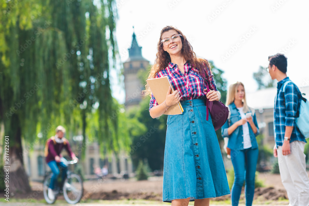 Fototapeta premium selective focus of smiling student with notebook and multicultural classmates behind on street