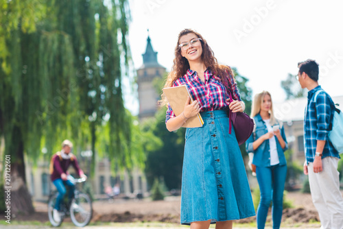 selective focus of smiling student with notebook and multicultural classmates behind on street