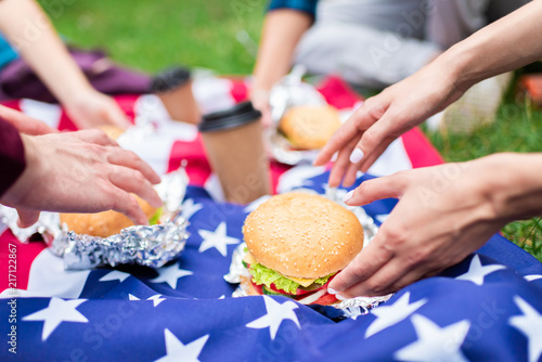 partial view of friends with burgers and american flag on green grass in park