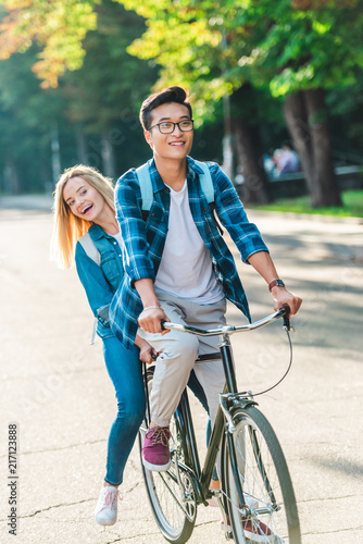 happy multiethnic students riding bicycle together on street