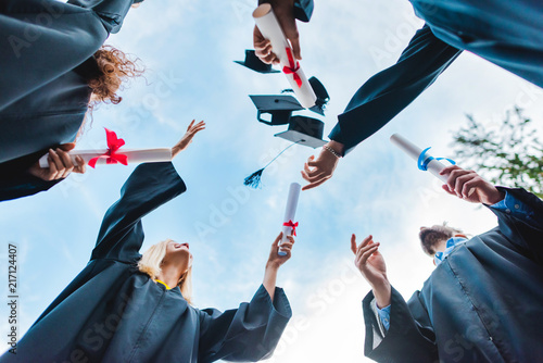 bottom view of happy multicultural graduates with diplomas throwing caps up with Fototapet