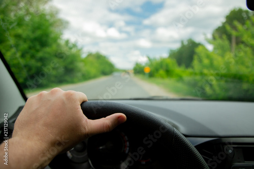 The driver's hands on the steering wheel of the car and an empty asphalt road. Road repair ahead