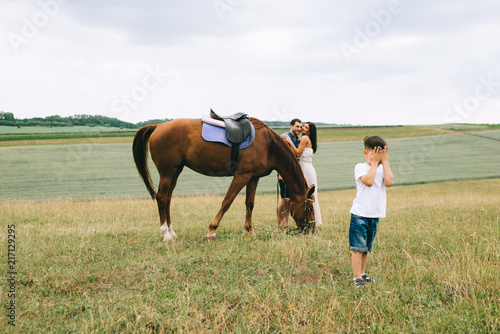 parents hugging near horse, son covering eyes on field
