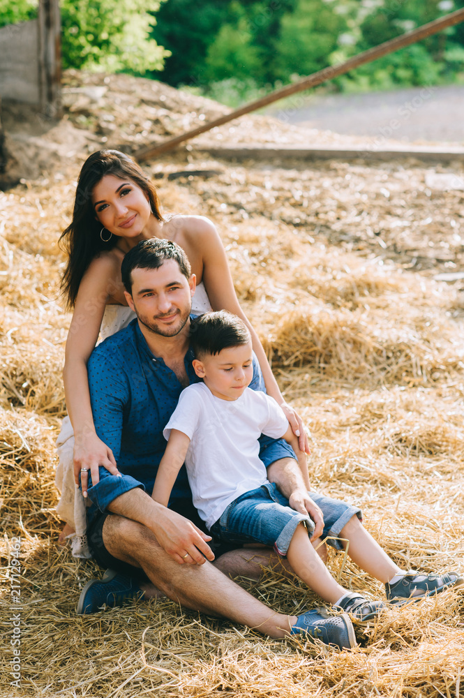 Fototapeta premium cheerful parents and son sitting on hay at village