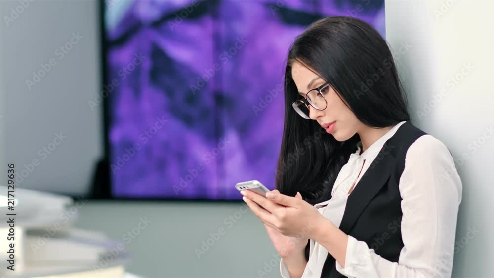 Attractive young businesswoman in glasses using smartphone at futuristic hi-tech exhibition Attractive young businesswoman in glasses using smartphone at futuristic hi-tech exhibition