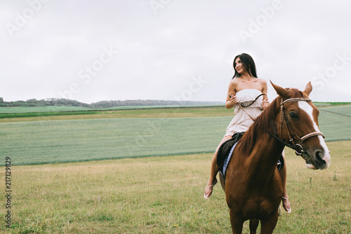 beautiful woman riding brown horse on field