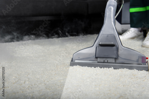 Close-up view of person cleaning white carpet with professional vacuum cleaner