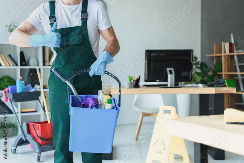 Cropped shot of professional cleaner holding bucket with cleaning supplies and showing thumb up