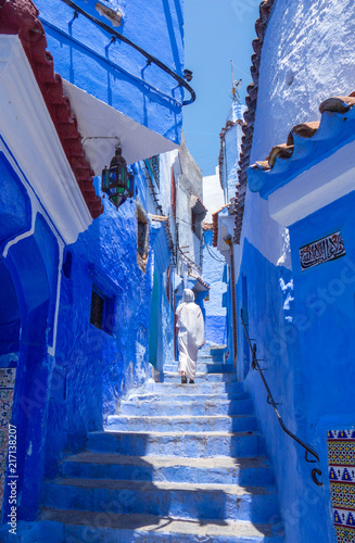 Woman with white djellaba walking the blue streets of Chefchaouen, Morocco. © Lia Aramburu