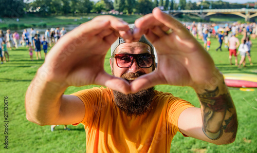 Man bearded hipster in front of crowd people show heart gesture riverside background. Hipster happy celebrate event picnic fest or festival. Urban event celebration. Cheerful fan love summer fest