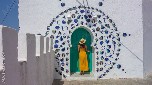 Woman in yellow dress and hat in a nice decorated door of the village of Asilah in Morocco