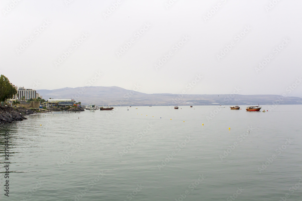 The calm waters of the Sea of Galilee with moored boats in early evening on a hazy day in May 2018 
