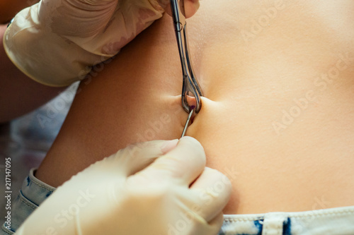 hand in a rubber glove close-up of master prepares to pierce the navel by belly of a young woman with a bandage and cotton on her stomach. process navel ring piercing concept