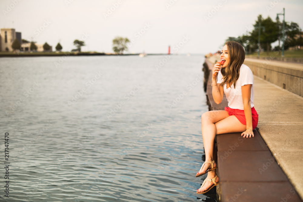 A beautiful, young woman enjoying ice cream by the marina