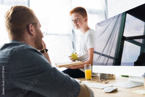son holding book and apple and looking at father at home