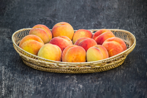 Fototapeta Naklejka Na Ścianę i Meble -  Fresh peaches in wicker basket on dark wood background