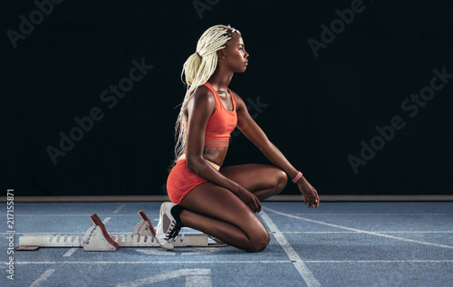Woman sprinter sitting at the start line on a running track