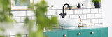 Real photo with blurred foreground of white bathroom interior with tiles, fresh plants and sink on green cabinet