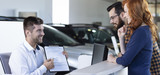 Panorama of smiling professional car dealer showing daily rental agreement to buyers