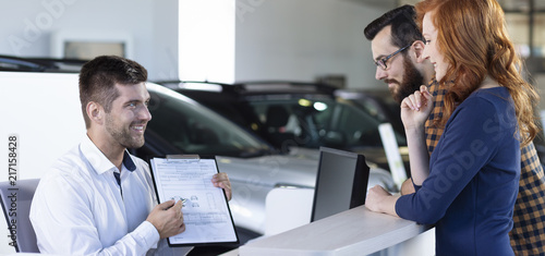 Panorama of smiling professional car dealer showing daily rental agreement to buyers