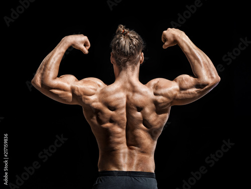 Young man showing his muscles. Rear view of bodybuilder with perfect physique on black background. Strength and motivation.