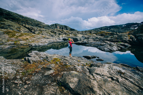 Travel in Norway, woman hiker in bright sportswear with backpack s relaxing and drinking water over scandinavian lake over mountains summer view background.