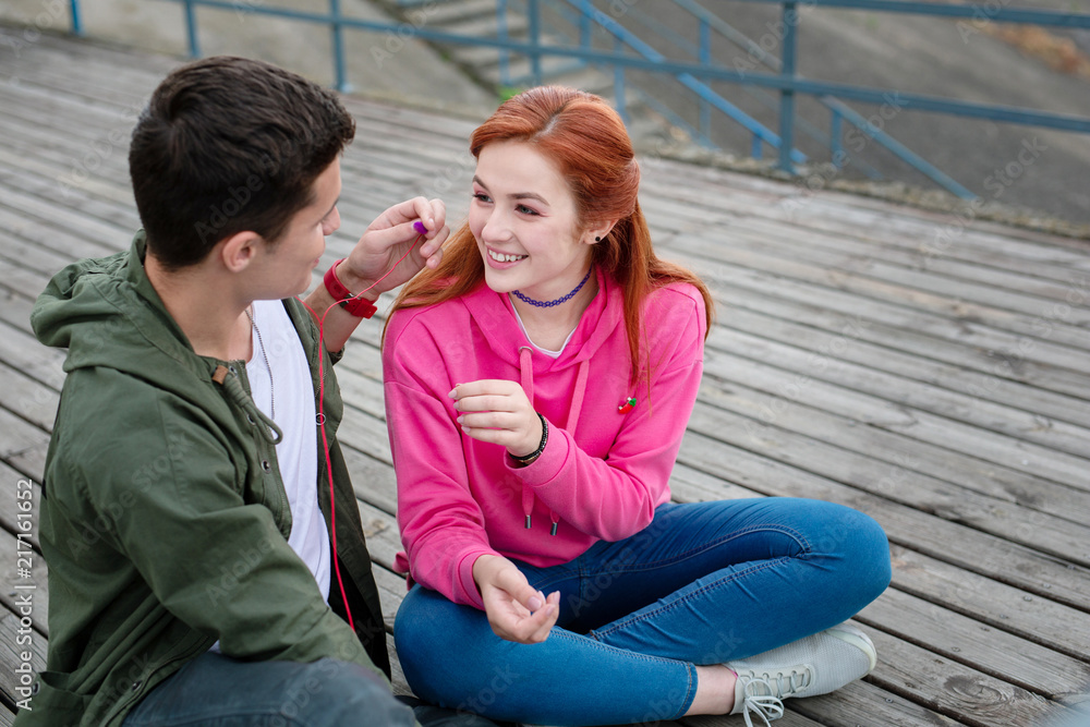 Obraz premium Music playlist. Pleasant young couple listening to music while sitting together on the dock