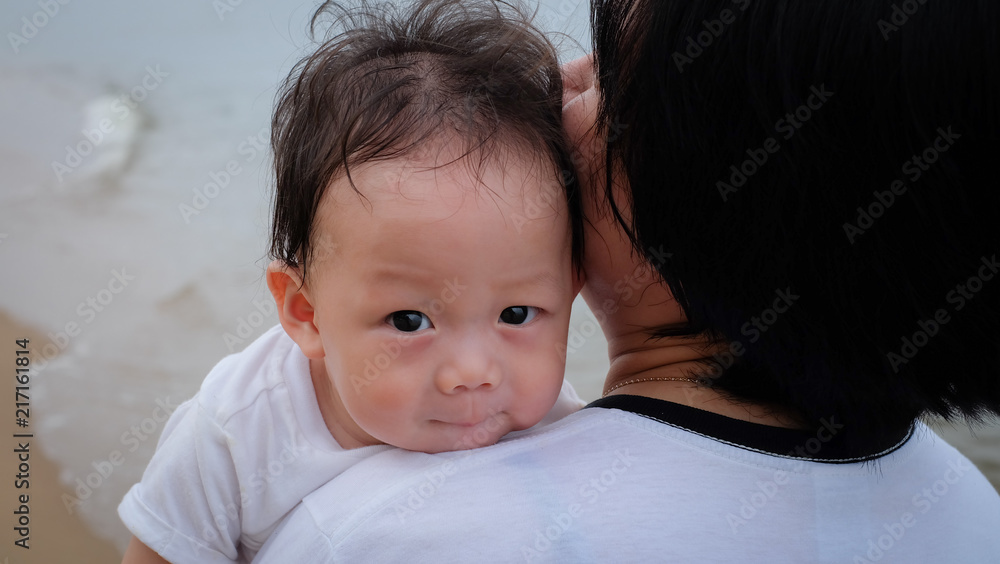 The Asian mother hold the little baby with sweet smile.They go for a walk on the sandy beach. The Asian mother hold the little baby with sweet smile.They go for a walk on the sandy beach.