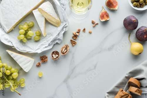 flat lay with cheese, wine and fruits arranged on white marble surface