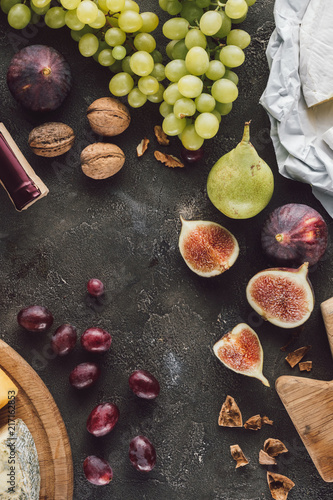 flat lay with arranged fruits, cheese and hazelnuts on dark surface