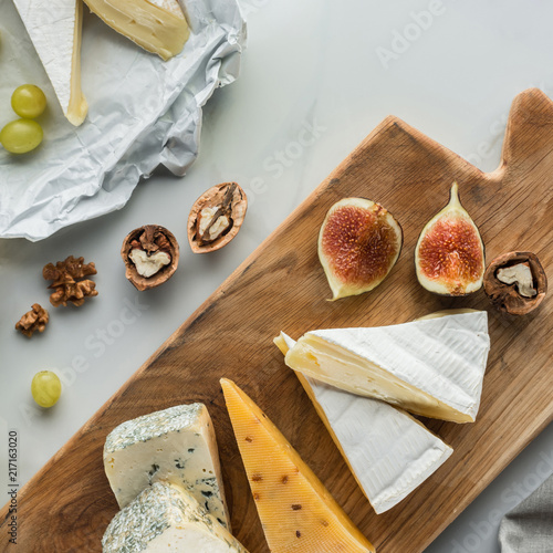 flat lay with food composition of cheese and fig pieces on cutting board on white marble surface photo