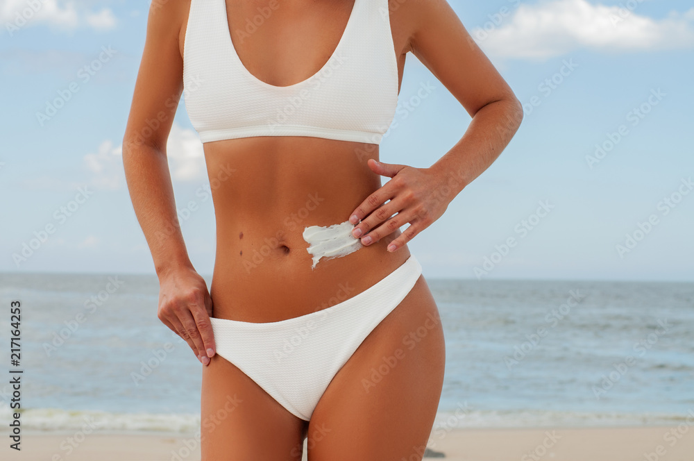 Beautiful woman on the beach in white swimsuit is applying sunscreen cream Beautiful woman on the beach in white swimsuit is applying sunscreen cream