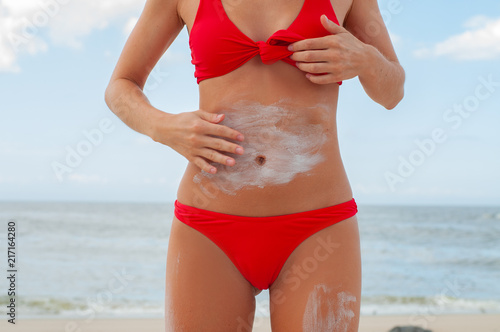 Beautiful woman on the beach in red swimsuit is applying sunscreen cream