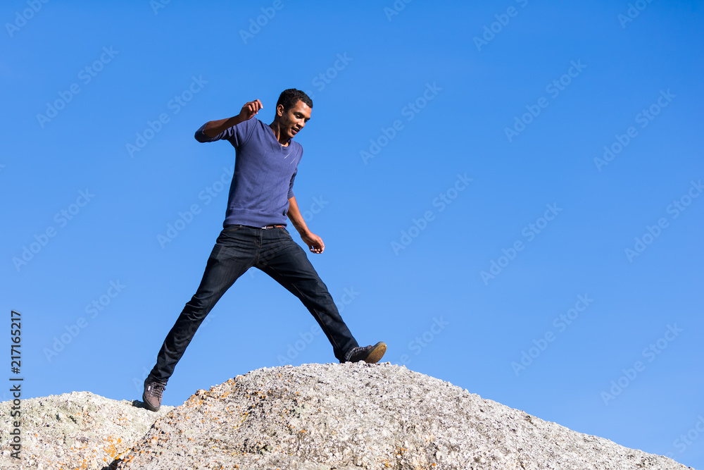 Obraz premium Young Man Taking Large Step Across Boulders