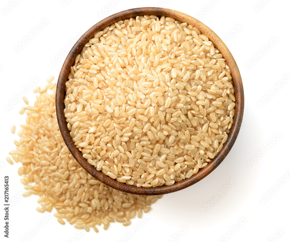 uncooked brown rice in the wooen bowl, isolated on the white background, top view uncooked brown rice in the wooen bowl, isolated on the white background, top view