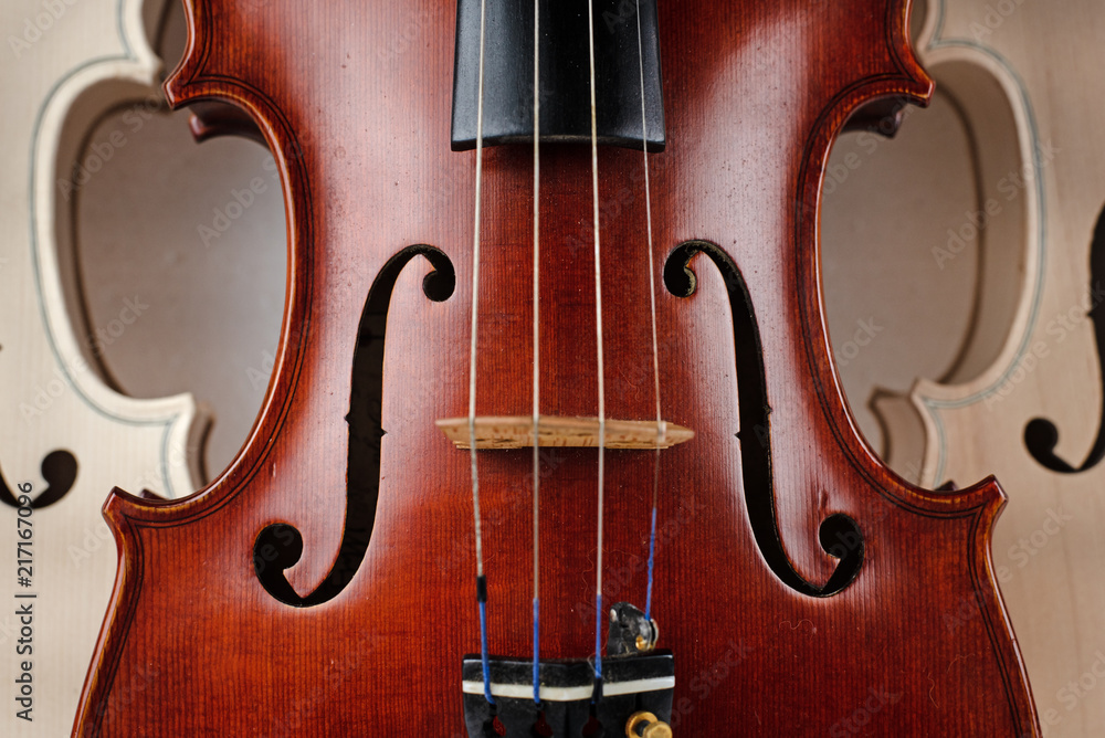 Closeup front side of completed violin,in front of half front side of raw violin,blurry light around