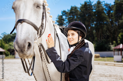 Fond of equestrianism. Beautiful beaming dark-haired woman with red nail art fond of equestrianism