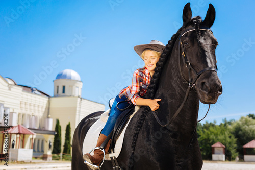 Cowboy girl. Cute cowboy girl wearing nice cowboy hat hugging her beautiful black horse