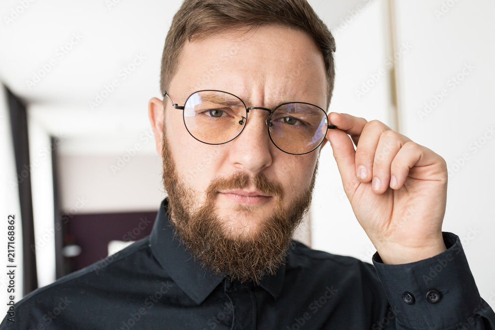 a white bearded man in round medical glasses and a black shirt looks carefully at the camera a white bearded man in round medical glasses and a black shirt looks carefully at the camera