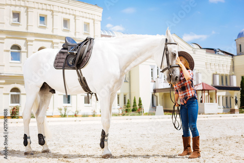 Kissing horse. Caring loving cowboy girl fond of equestrianism kissing her beautiful white racing horse