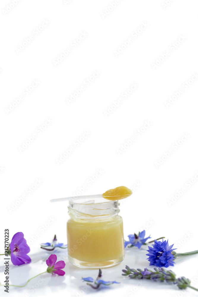 Raw organic royal jelly on white board surrounded by flowers on white background Raw organic royal jelly on white board surrounded by flowers on white background