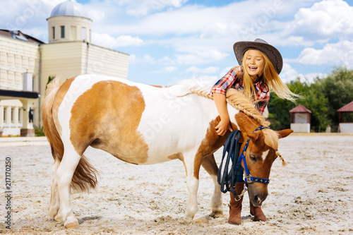 Fun with pony. Amused cowboy girl feeling very memorable and cheerful while having fun with pony outside stable