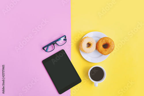 Home office, Cup of coffee, donuts, eye glasses and tablet on pastel background with copy space