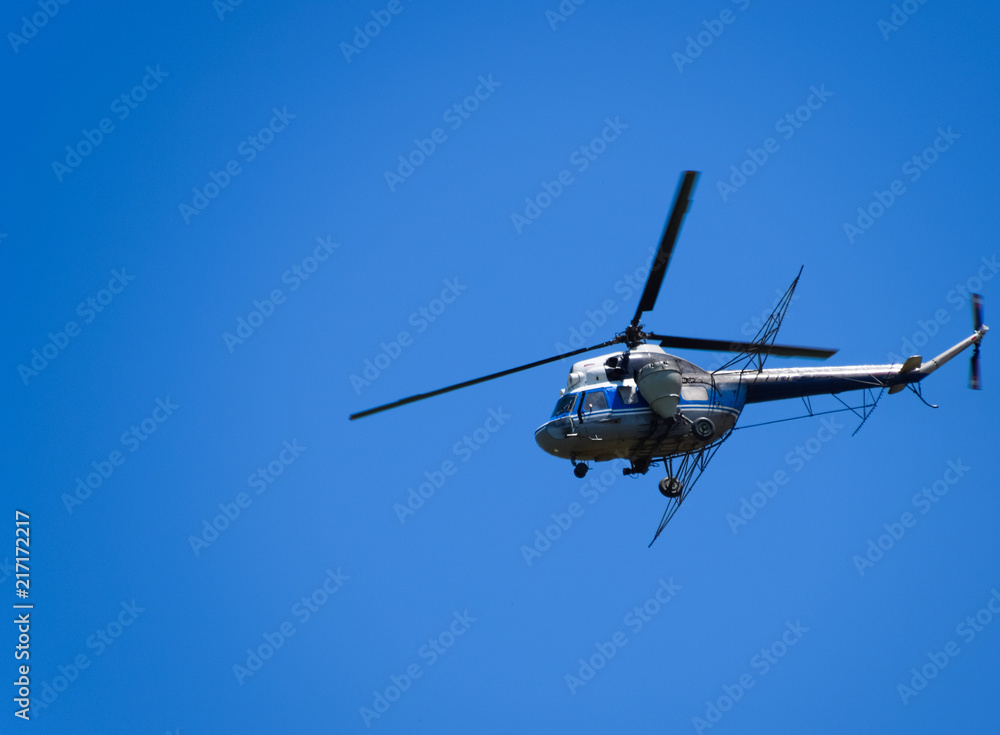 A helicopter of agricultural aviation is flying in the blue sky.