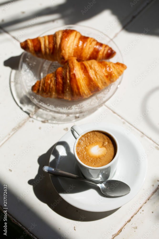 Hot coffee and croissant breakfast in a sunny morning, natural light.