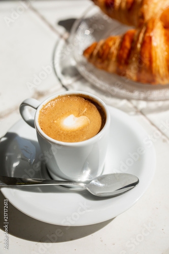 Hot coffee and croissant breakfast in a sunny morning, natural light.