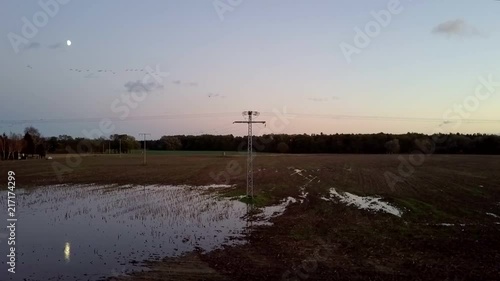 Drone Shot at Sunset look at a Electrictower shaped like a cross and brids flying by. photo