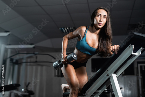 Woman trains in the gym. Athletic woman trains with dumbbells, pumping his biceps