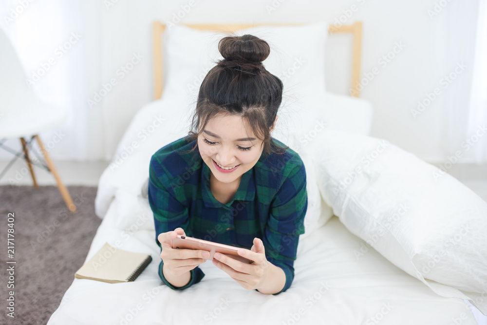 Cute Woman use of mobile phone in bedroom and smile. happy Asian girl play game on smartphone Cute Woman use of mobile phone in bedroom and smile. happy Asian girl play game on smartphone